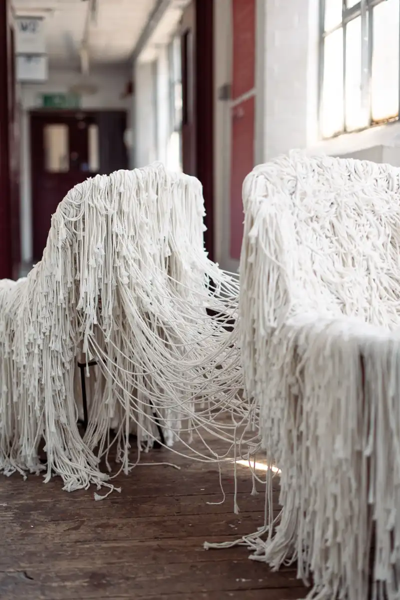 Two pale woven chairs entangled with each other, fibres running between them