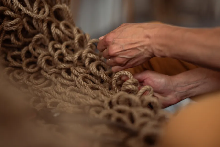 Close view of hands knotting heavy rope into a woven structure