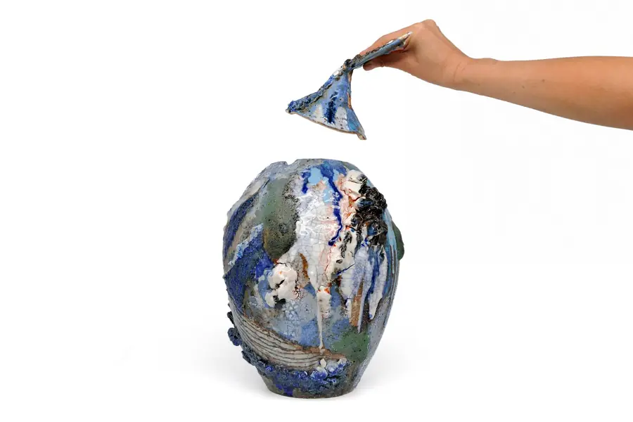 A hand lifting the whale tail lid off a jar
